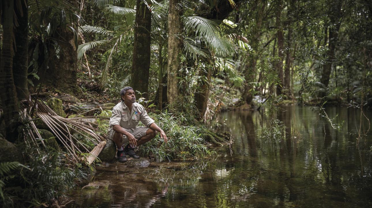 A guide crouching by the side of a river