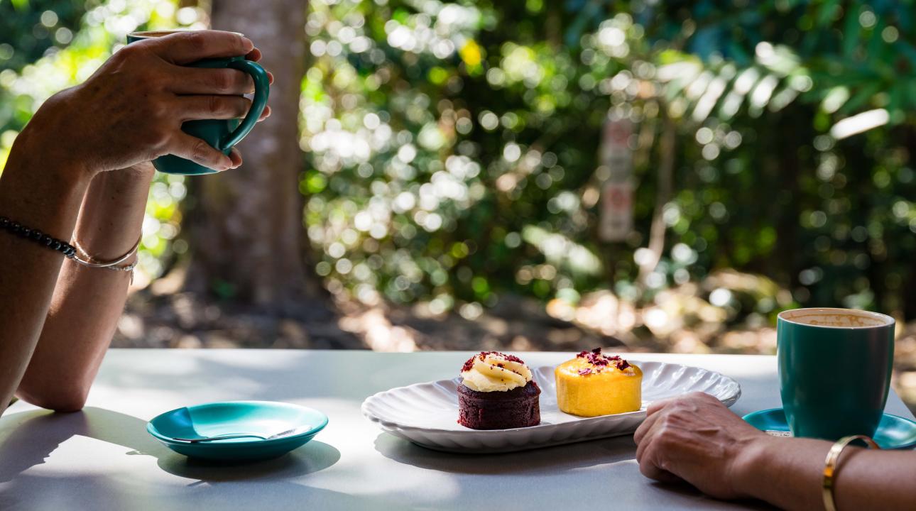Two people sitting at a table outside drinking coffee and eating cakes at Mayi Cafe and Restaurant