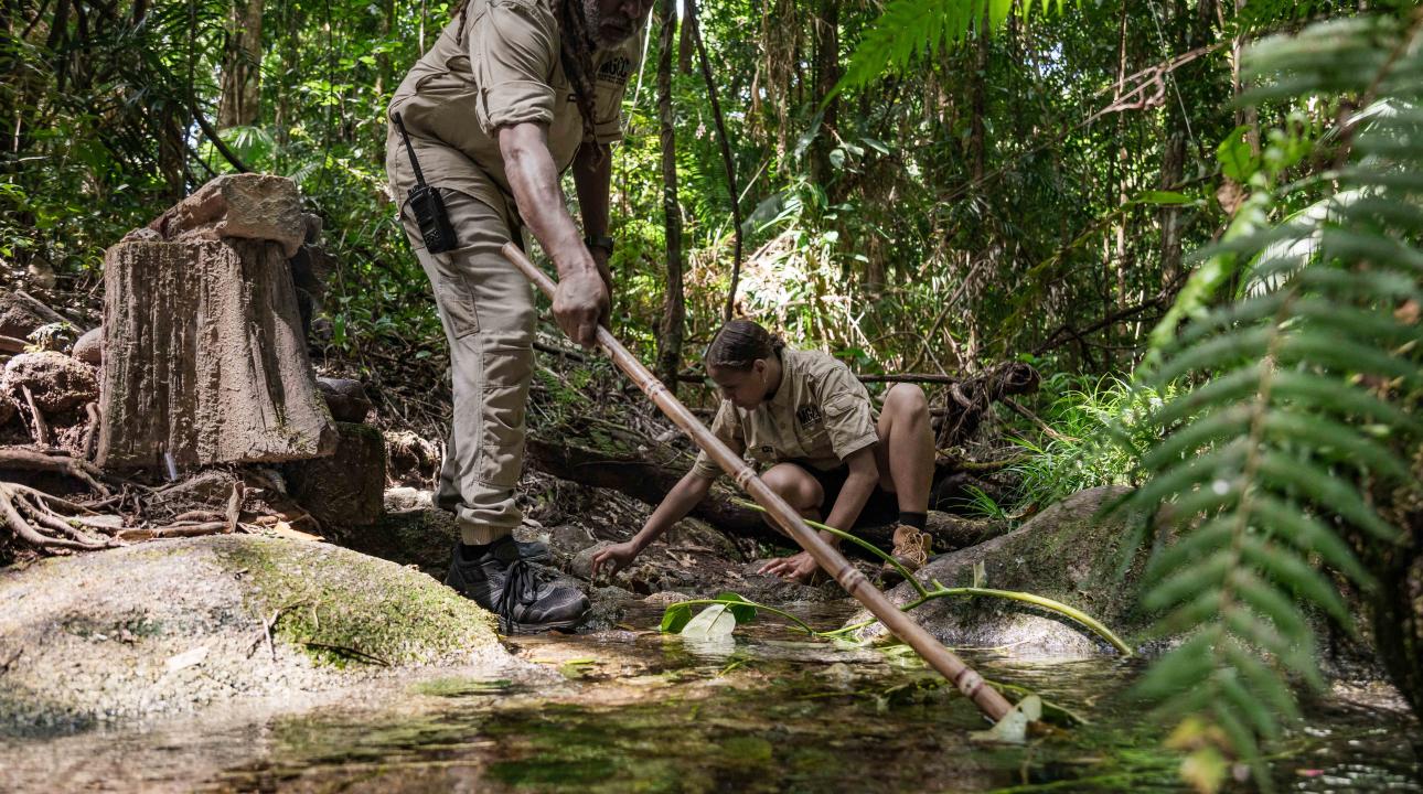 Guides in front of a water hole touching the rainforest floor