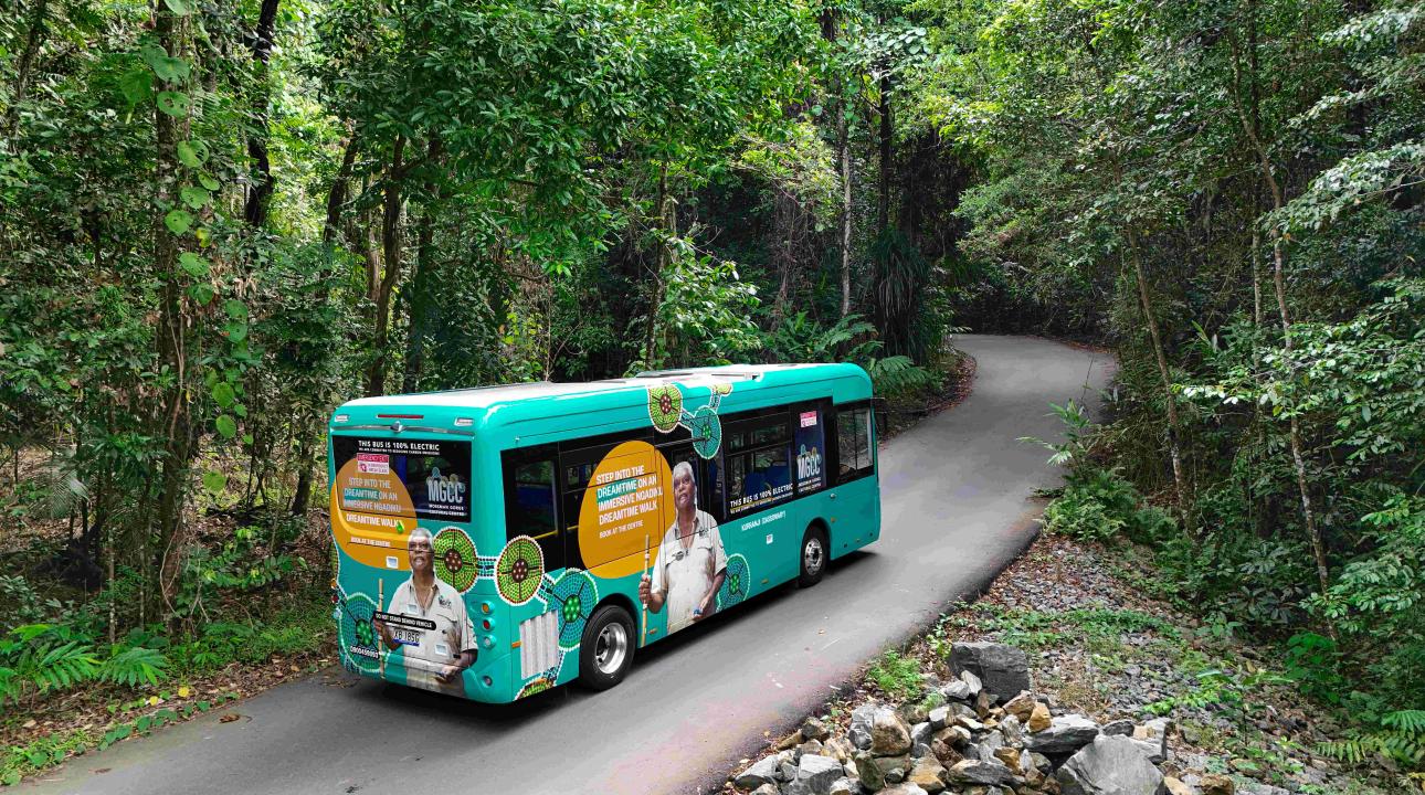 EV Shuttle bus with Mossman Gorge Cultural Centre Branding driving down a road in the Daintree Rainforest