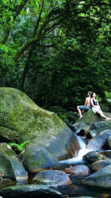 Couple sitting back to back on some rocks by the river